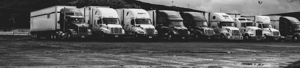Row of parked semi trucks in a rainy lot, captured in a dramatic black and white setting.